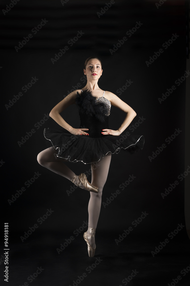 Beautiful ballerina in the role of a black swan, wearing black tutu and pointe shoes on black background