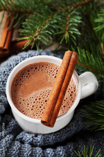 Cup of hot cocoa or hot chocolate on knitted background with fir tree and cinnamon sticks, traditional beverage for winter time