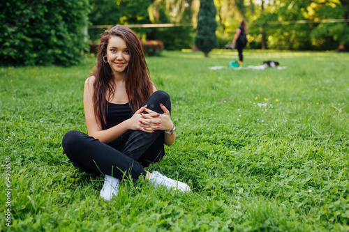 Brown hair girl spending free time, sitting on the grass in the park. © jakubzak