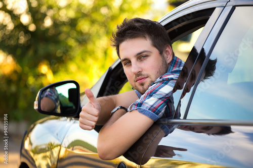 Young man smiling and showing thumbs up in his car