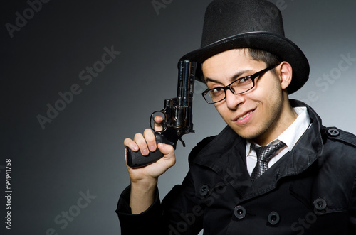 Criminal in black coat holding hadgun against gray