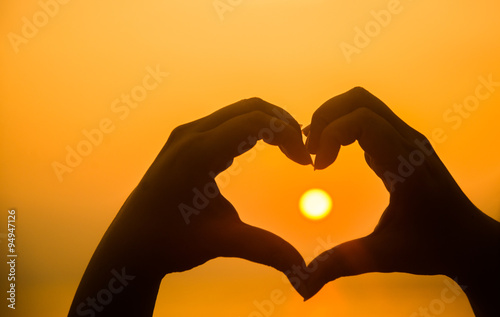 hand making heart shape over sunset