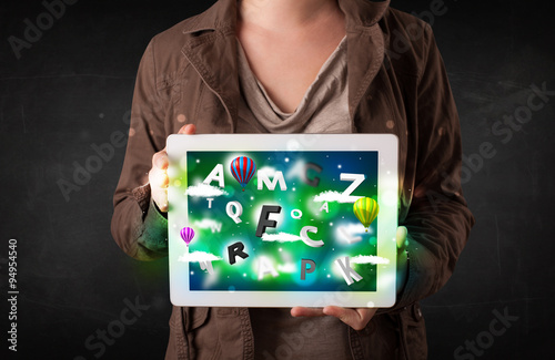 Young person showing tablet with abstract letters and sky