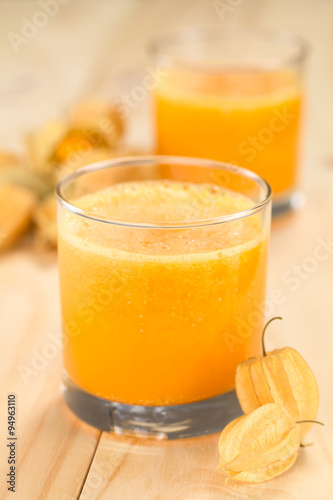 Freshly prepared juice made of physalis (lat. Physalis peruviana) served in glass (Selective Focus, Focus on the front of the glass rim and on the front of the first physalis next to the glass)