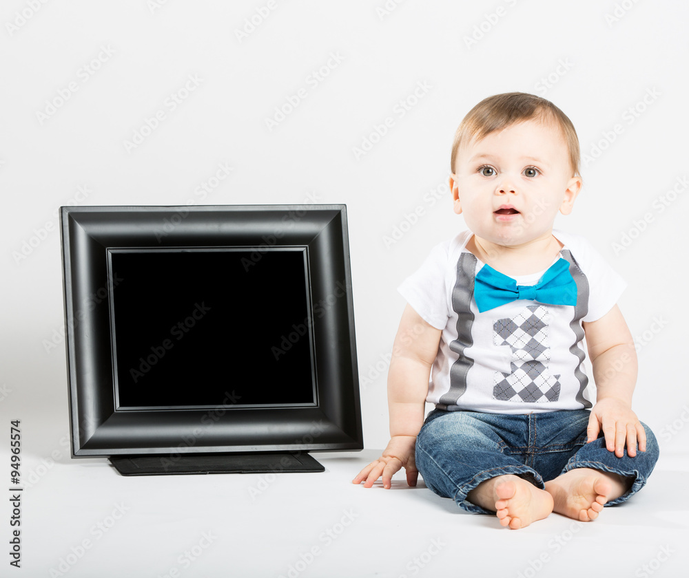 a cute 1 year old baby sits next to a blank black picture frame in a