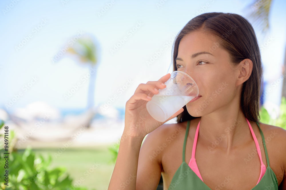 Young woman drinking fresh water or lime juice at beach. Female is looking away while sitting at outdoor restaurant. Beautiful tourist is having healthy drink during summer vacation. Young woman drinking fresh water or lime juice at beach. Female is looking away while sitting at outdoor restaurant. Beautiful tourist is having healthy drink during summer vacation.