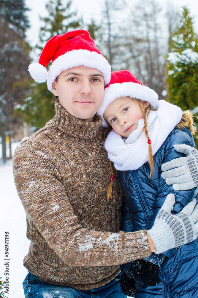 Happy father and little girl in Santa hats with christmas tree outdoors