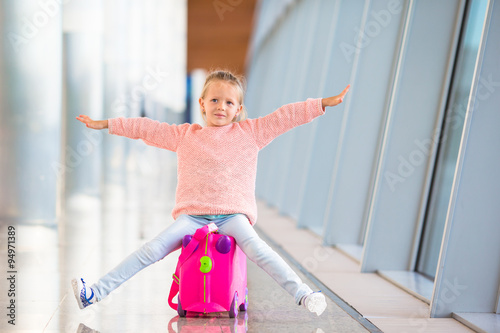 Fototapeta Naklejka Na Ścianę i Meble -  Adorable little girl having fun in airport sitting on suitcase