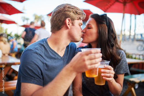 couple with draft beers kissing at outdoor pub or bar patio shot with selective focus