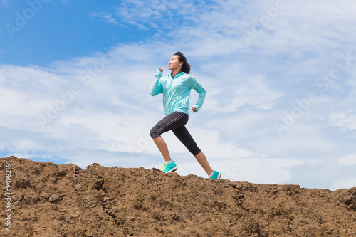 young woman running on trail with blue sky background