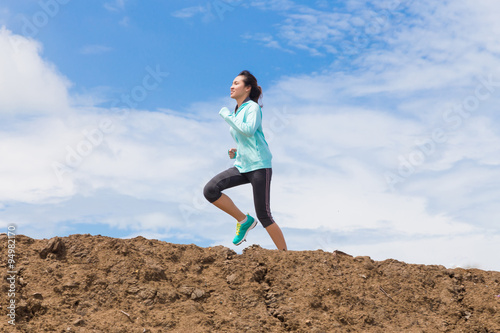 young woman running on trail with blue sky background