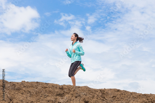 young woman running on trail with blue sky background