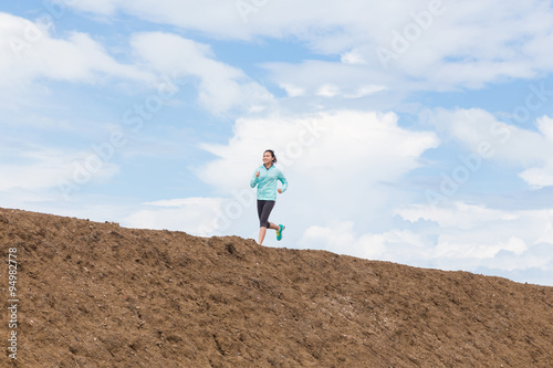 young woman running on trail with blue sky background
