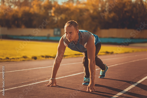 Athletic man standing in posture ready to run on a treadmill.