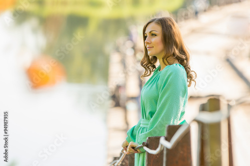 Beautiful girl standing on the bridge over the river and looks into the distance