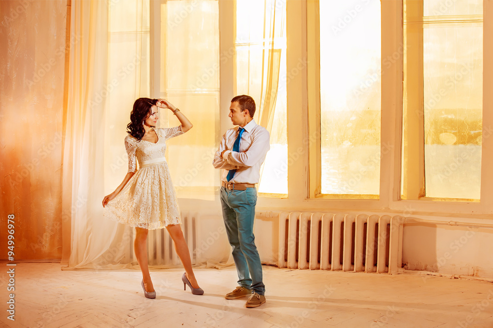 Beautiful young couple is standing at summer golden sunset window