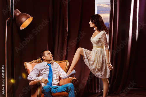 Beautiful young woman is flirting with man sitting on armchair 