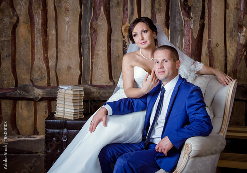 Studio portrait of bride and groom sitting relaxed on the armchair on their wedding day, vintage interior © elenakirey