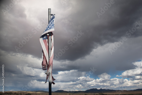 Close-up of a tattered American Flag on an aging flagpole in a rural landscape on a cloudy day, USA