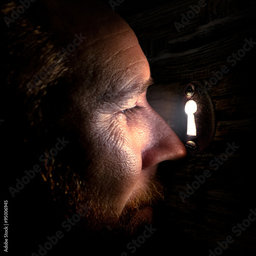 Close-up of a man looking through a keyhole in a door spying photo