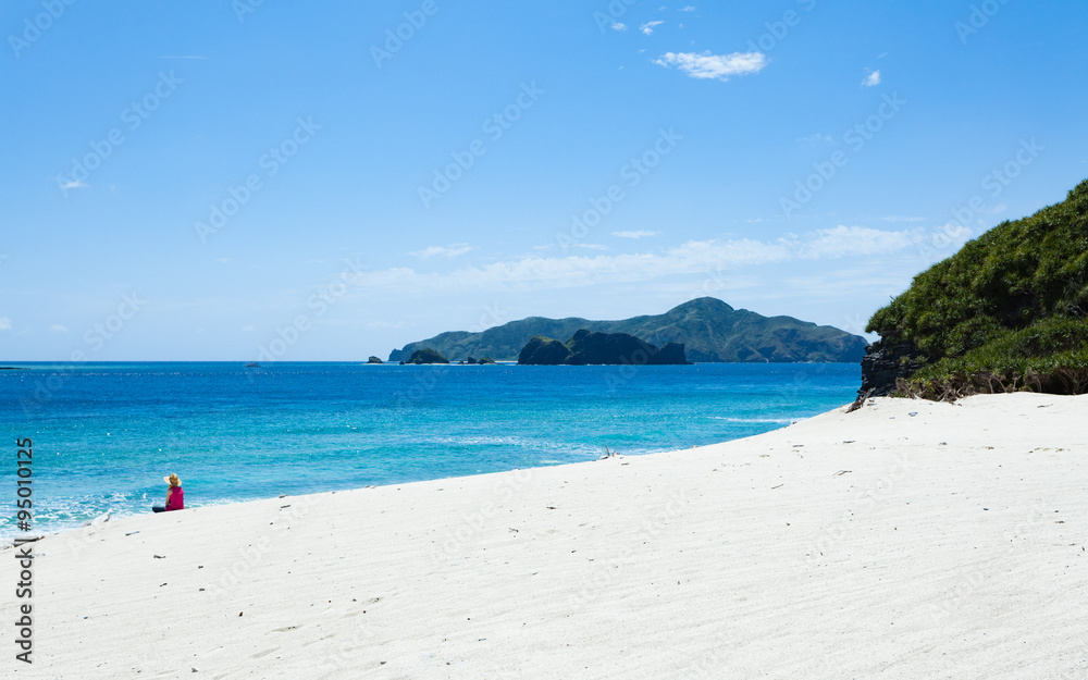 Woman sitting on deserted tropical island beach, Okinawa, Japan
