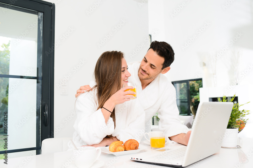 young couple in bathrobe at home having coffee in the kitchen and working on laptop computer young couple in bathrobe at home having coffee in the kitchen and working on laptop computer
