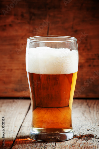 large glass of light beer with foam on the old wooden background