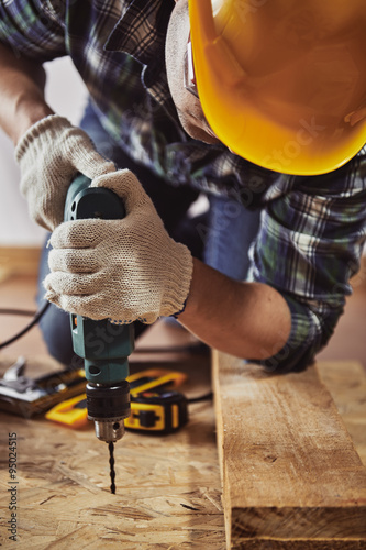 Young handyman in hardhat drilling wood in working studio. Concept of craft and technology.