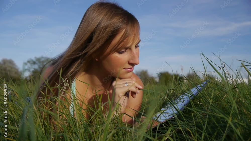 DOLLY: Girl lying in meadow using a digital tablet DOLLY: Girl lying in meadow using a digital tablet