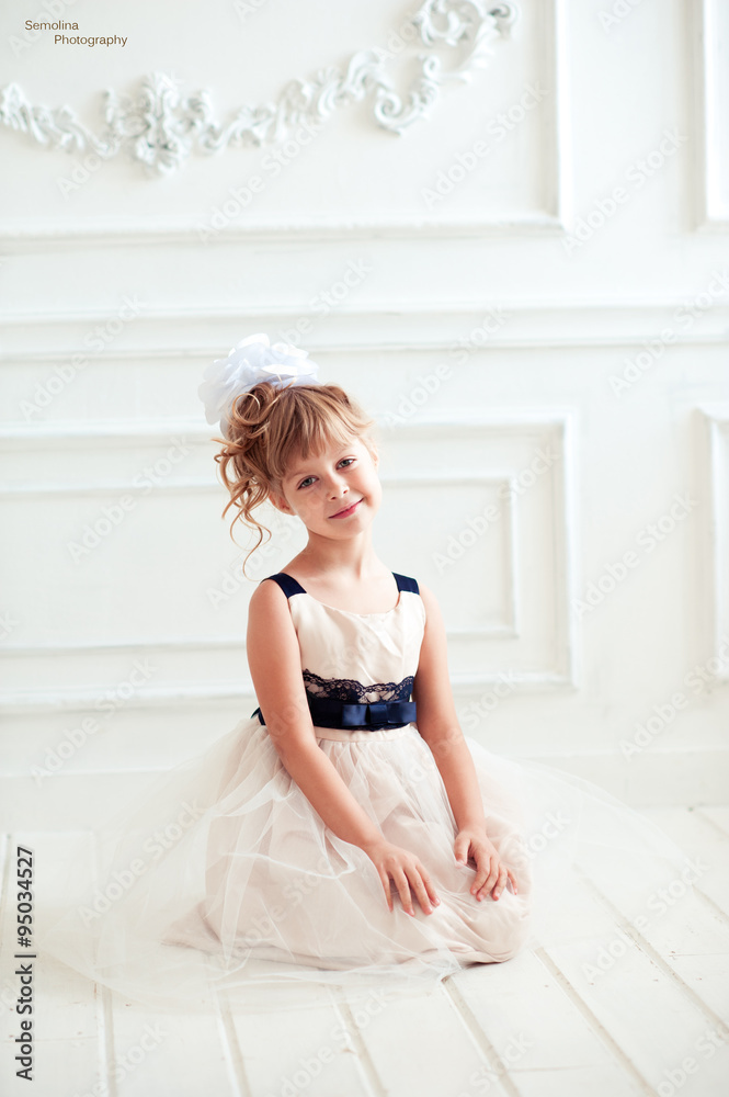 Smiling baby girl 4-5 year old wearing stylish dress in room. Sitting on wooden floor. Looking at camera. Childhood. Smiling baby girl 4-5 year old wearing stylish dress in room. Sitting on wooden floor. Looking at camera. Childhood.