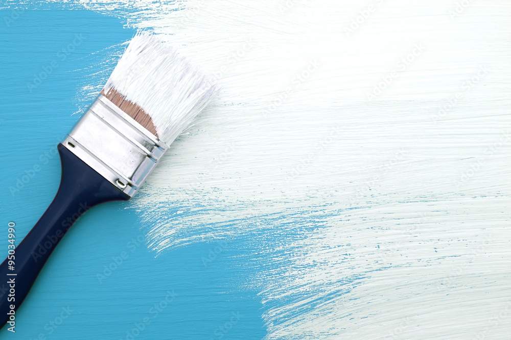 Obraz premium Paintbrush with white paint painting over blue