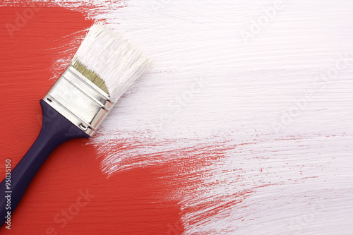 Paintbrush with white paint painting over red