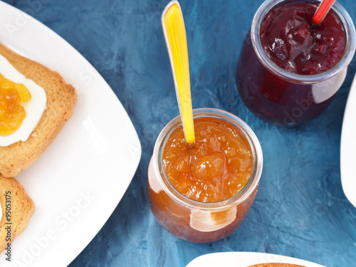 Apricot and cherry jam in glass cups on blue background photo