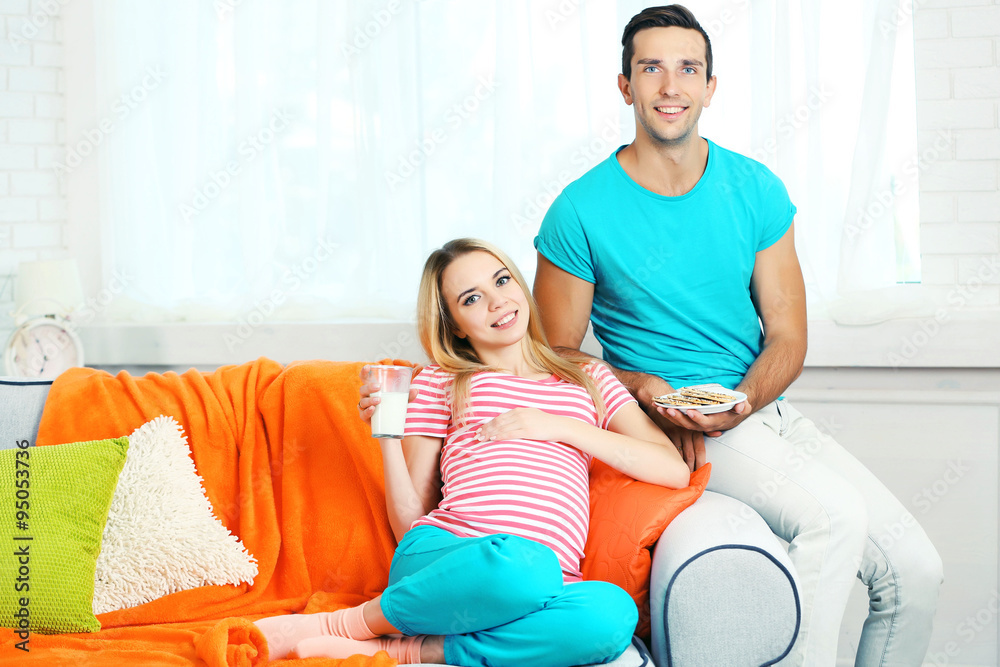 Young pregnant woman with husband on sofa in room Young pregnant woman with husband on sofa in room
