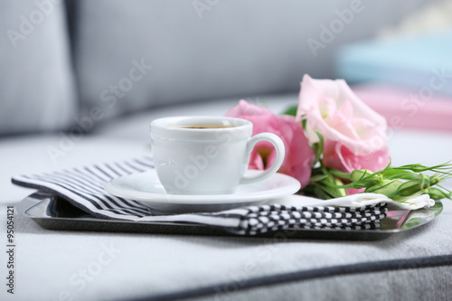 Cup of coffee with flowers on tray on sofa in room