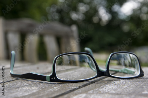 Abandoned glasses on a wooden garden table. Black and green frame. Blurred green background.