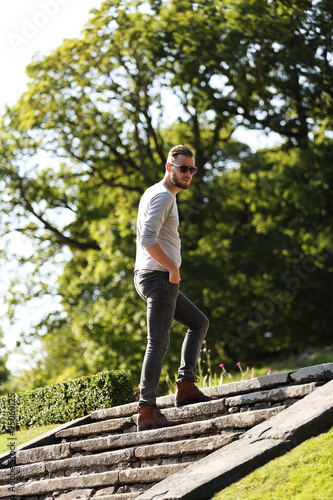 Man wearing jeans,boots and a grey shirt walking up a stone steps outside on a sunny summer day.  © _robbie_