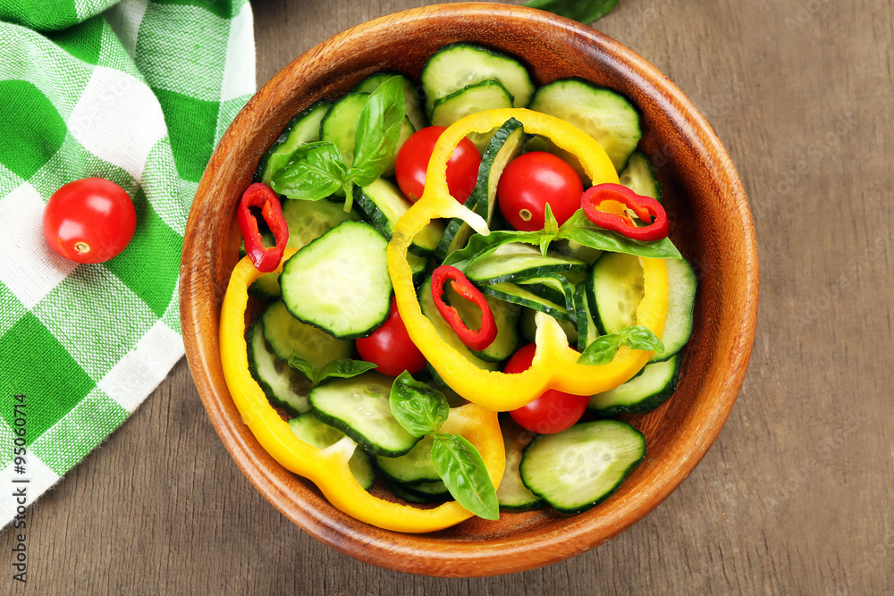 Vegetable salad with cucumbers  on wooden background decorated with green checked cotton serviette and sweet pepper