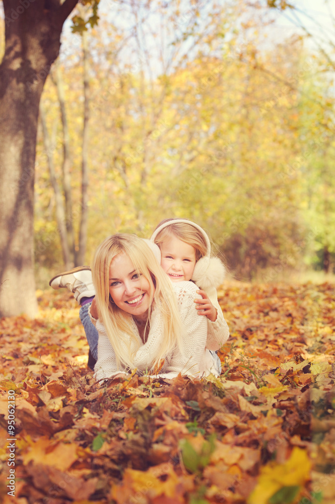 Smiling happy cute mother and little daughter lying on yellow maple leaves. Smiling happy cute mother and little daughter lying on yellow maple leaves.