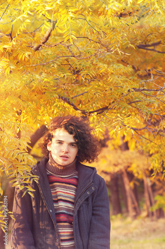 Young attractive calm man portrait dressed in gray jacket and striped sweater, standing in autumn park.