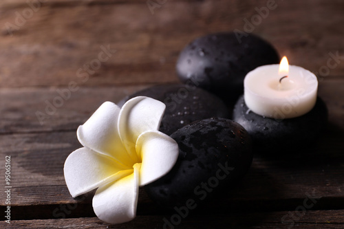 Relaxing concept - fragipani flower, pebbles and candles on wooden background
