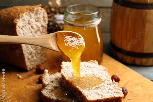 Fototapet Honey dripping on fresh bread on wooden background