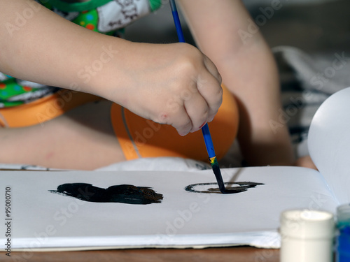 Маленький ребенок рисует кистью с черной краской рисунок на листе бумаги. Акварель, гуашь. Малыш учится рисовать 