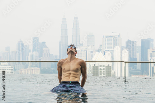 young attractive man at the swimming pool in roof at skyscraper.