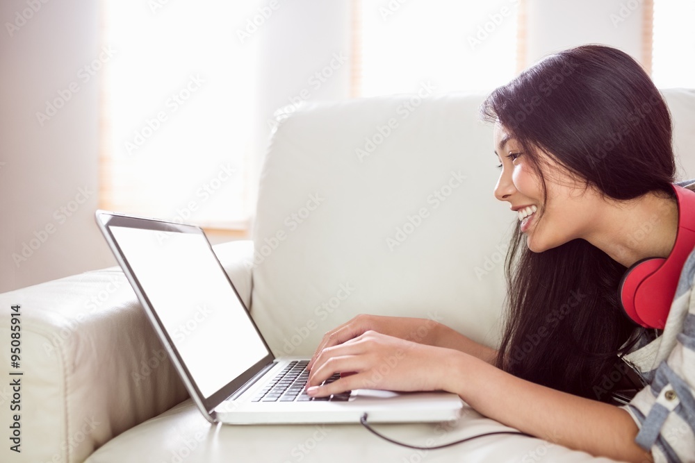 Smiling asian woman on couch using laptop Smiling asian woman on couch using laptop