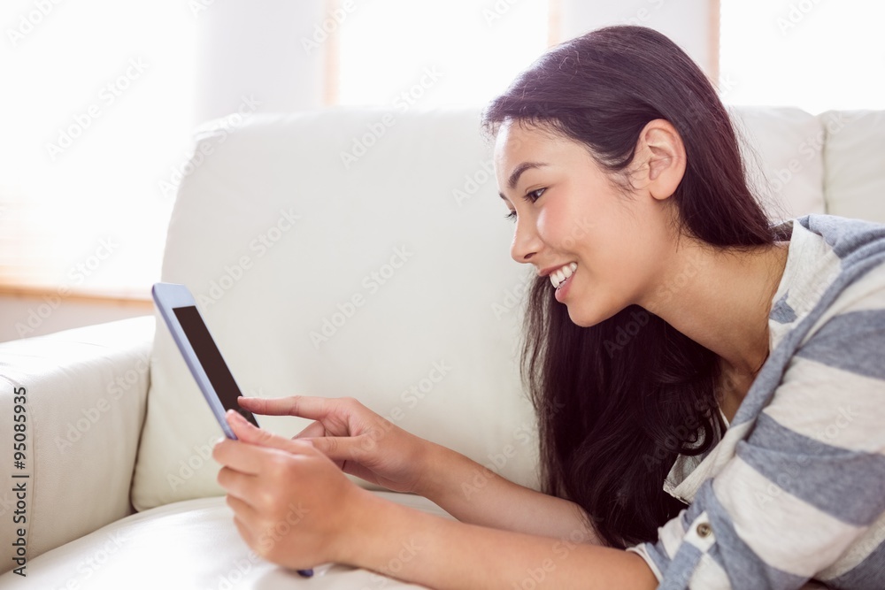 Smiling asian woman on couch using tablet Smiling asian woman on couch using tablet