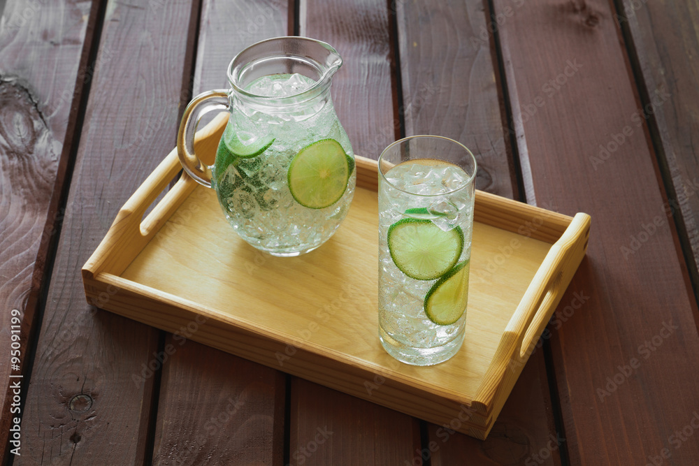 Drink and jug on wooden tray with ice and condensation on glass