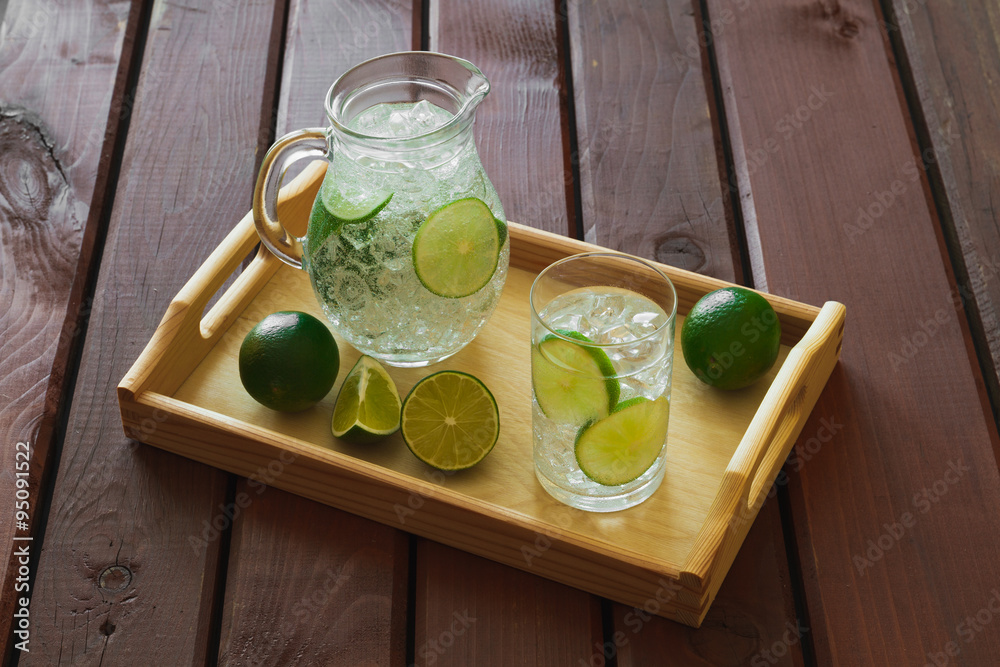 Drink and jug on wooden tray with ice and condensation on glass