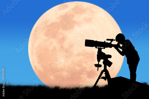silhouette of little boy looking through a telescope at the full