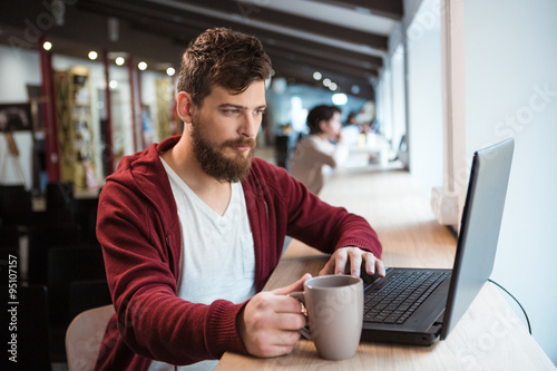 Handsome hipster using laptop and drinking coffee